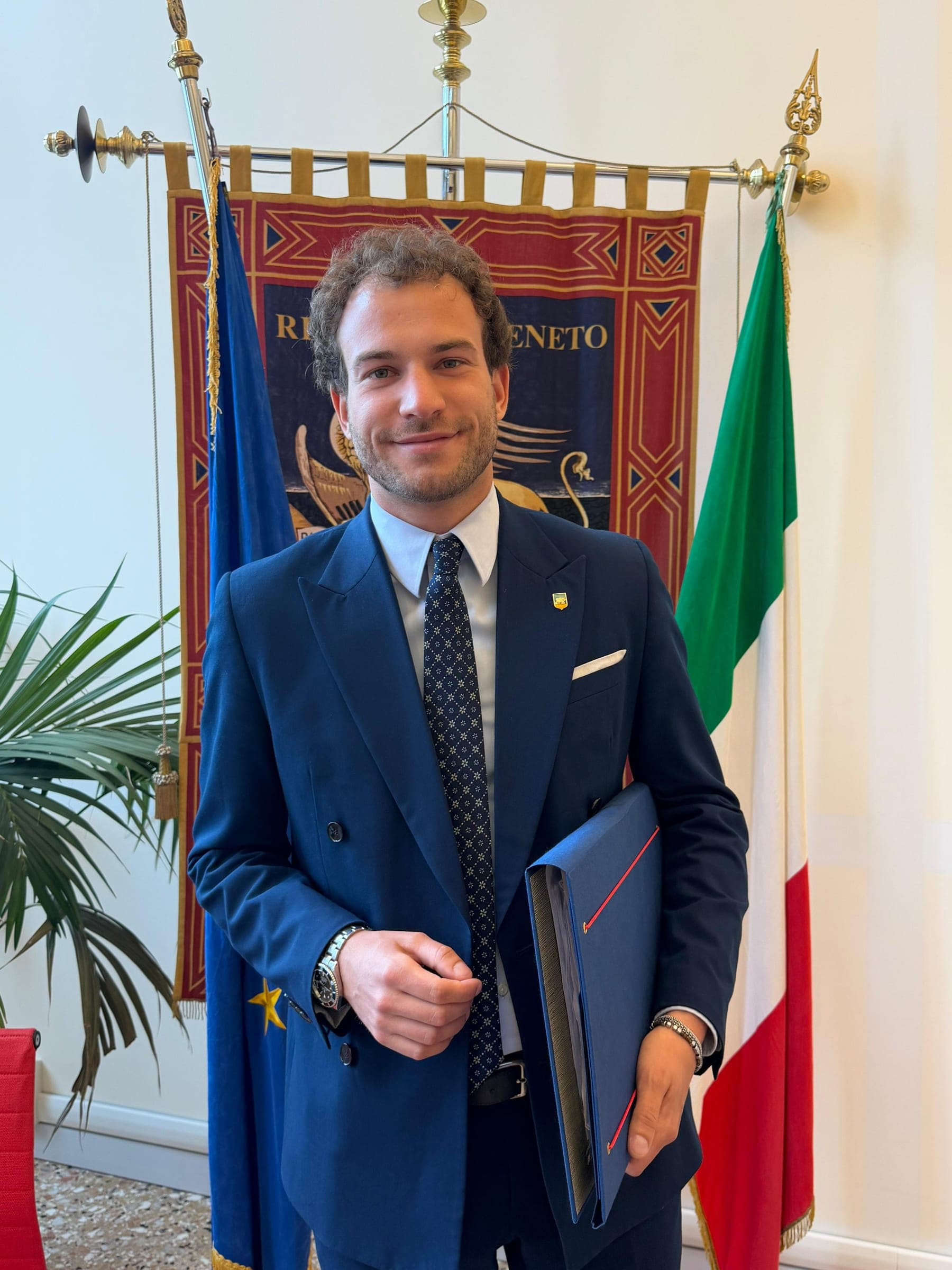 Jacopo Maltauro davanti al gonfalone della Regione del Veneto, tra la bandiera europea e il tricolore